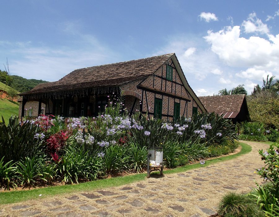 Casa enxaimel de dois andares com vigas de madeira escura formando triângulos sobre parede clara.