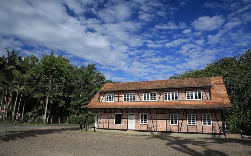 Casa enxaimel branca com estrutura de madeira escura e jardim bem cuidado, em Pomerode.