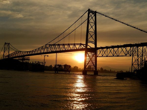 Ponte Hercílio Luz iluminada ao anoitecer, ligando a ilha ao continente.