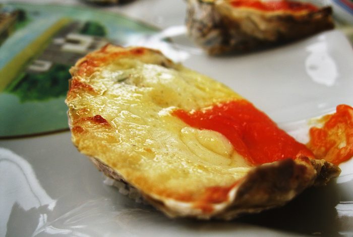 Ostras gratinadas em conchas, servidas quentes em prato branco.