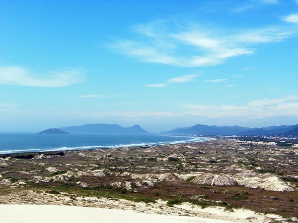Dunas de areia clara com mar ao fundo na Praia da Joaquina, Florianópolis.