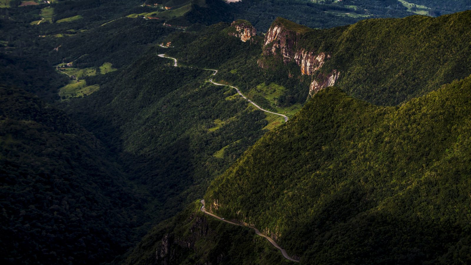 Estrada sinuosa descendo uma serra alta entre paredões de rocha e nuvens baixas.