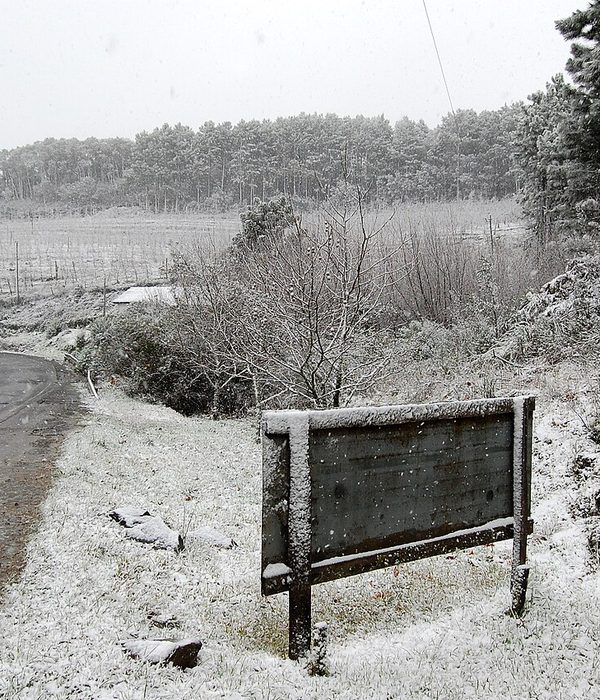 Paisagem rural com camada fina de neve sobre a grama e cercas de madeira.